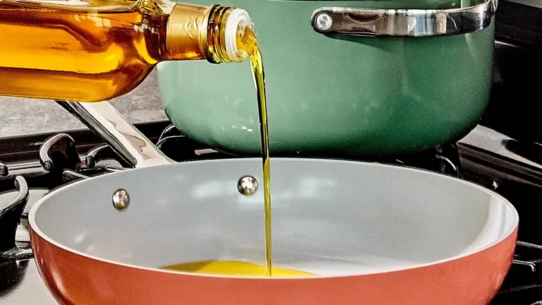 Olive oil being poured into a rust-colored frying pan on a stove.